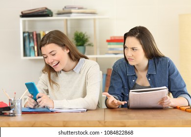 Angry student looking at her lazy mate who is playing with the smart phone instead of working