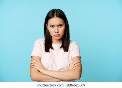 Angry teen asian girl standing in offended pose, frowning and sulking, feeling defensive, standing disappointed over blue background - Shutterstock ID 2086625509