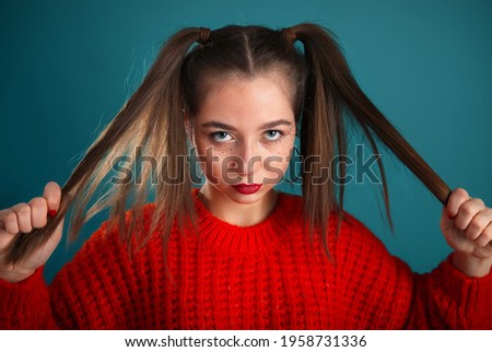 Angry teenager girl face portrait with long hair in hands. Teenager kid in red sweeter looking into the camera.