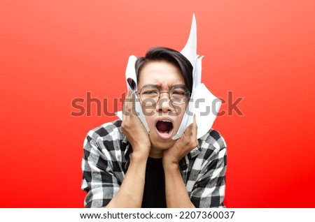 angry and tired of asian man student bite essay thesis paper work isolated over red. asian man stressed over work.