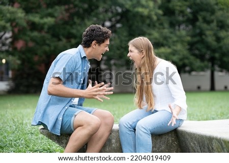 Angry and toxic couple shouting each other outdoors in a park. Relationship in adolescence concept.