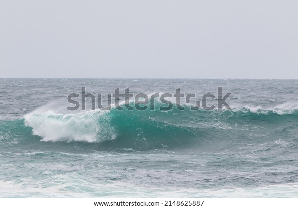 An angry turquoise green color massive rip curl of\
a wave as it barrels rolls along the ocean. The white mist and\
froth from the wave are foamy and fluffy. The ocean in the\
background is deep blue. 