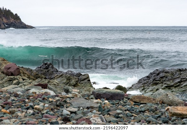 An angry turquoise green color massive rip curl of\
a wave as it barrels rolls along the ocean. The white mist and\
froth from the wave are foamy and fluffy. The ocean in the\
background is deep blue. 