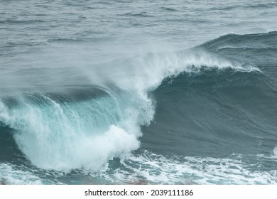 An Angry Turquoise Green Colour Massive Rip Curl Of A Wave As It Barrel Rolls Along The Ocean. The White Mist And Froth From The Wave Are Foamy And Fluffy. The Ocean In The Background Is Deep Blue. 