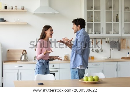 Angry unhappy young european woman and man fighting, screaming and gesturing in minimalist kitchen interior. Divorce, crisis, relationship problems, scandal and quarrel at home, conflict due covid-19