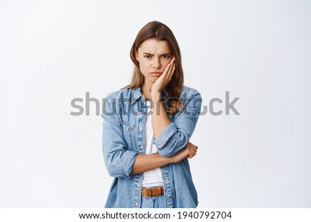 Angry and upset blond girl frowning, looking with dismay and hate, sulking and staring at camera something unfair and disappointing, standing against white background