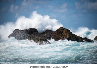 An angry wave crashing against large rocks in the sea under a cloudy sky on a stormy day