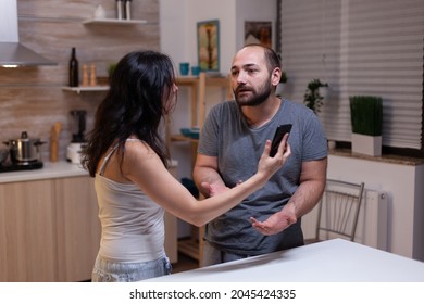 Angry Wife And Husband In Conflict Because Of Cheating. Man With Secret Lover Caught By Woman With Smartphone Messages. Couple Fighting About Marriage Infidelity And Jealousy Crisis