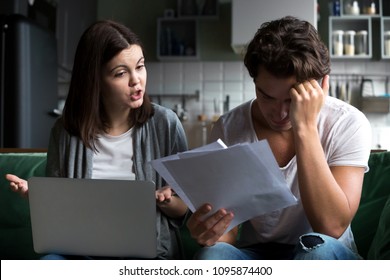 Angry Wife Scolding Blaming Upset Husband Of Unpaid Bills, Bankruptcy Or Past Due Debt, Unhappy Millennial Couple Having Financial Problems Arguing At Home Sitting On Sofa With Laptop And Papers