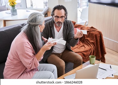 Angry Wife Scolding Blaming Upset Husband Of Unpaid Bills, Bankruptcy Or Past Due Debt. Unhappy Millennial Couple Having Financial Problems And Arguing At Home While Sitting On Sofa With Laptop And