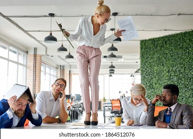 Angry Woman Boss Criticizing Frustrated Employees At Work Place In The Office, Blonde Female Stand On The Table Shouting