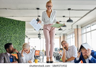 Angry Woman Boss Criticizing Frustrated Employees At Work Place In The Office, Blonde Female Stand On The Table Shouting