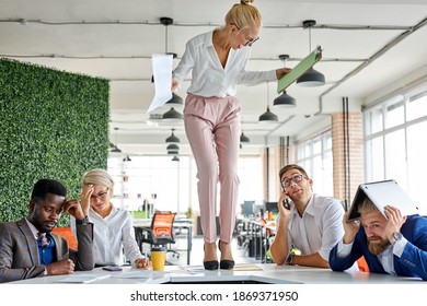 Angry Woman Boss Criticizing Frustrated Employees At Work Place In The Office, Blonde Female Stand On The Table Shouting