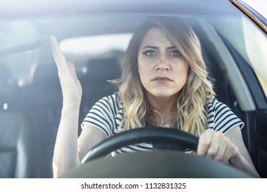 Angry woman driving a car. The girl with an expression of displeasure is actively gesticulating behind the wheel of the car.
