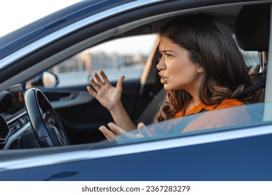 Angry woman driving a car. The girl with an expression of displeasure is actively gesticulating behind the wheel of the car. Angry business woman in a car. Stress girl in a car - Shutterstock ID 2367283279