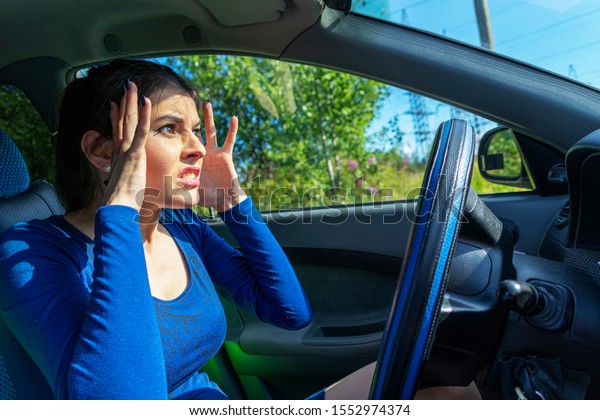 Angry woman driving a car. The girl with an\
expression of displeasure is actively gesticulating behind the\
wheel of the car. Car insurance\
concept