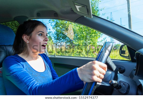 Angry woman driving a car. The girl with an\
expression of displeasure is actively gesticulating behind the\
wheel of the car. Car insurance\
concept
