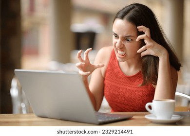 Angry woman having problems with a laptop in a bar terrace 