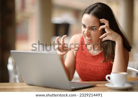 Angry woman having problems with a laptop in a bar terrace 