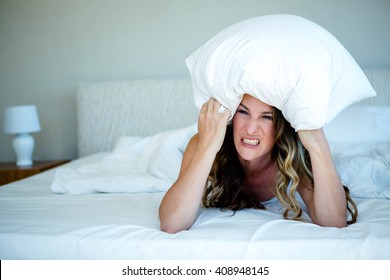 Angry Woman Lying On A Bed With A Pillow Over Her Head