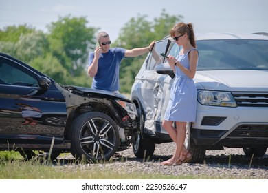 Angry woman and man drivers of heavily damaged vehicles calling insurance service for help in car crash accident on street side. Road safety concept - Shutterstock ID 2250526147