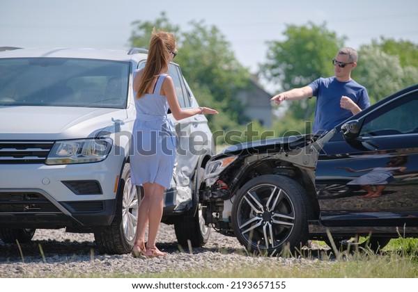 Angry woman and man drivers of heavily\
damaged vehicles arguing who is guilty in car crash accident on\
street side. Road safety and insurance\
concept