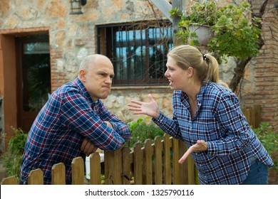 Angry Woman Quarreling With Her Male Neighbor, Talking Through Wooden Fence 

