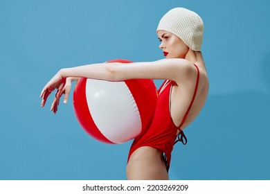 Angry woman in a red swimsuit with a swimming cap posing with a striped ball on a blue background. Abstract art concept - Powered by Shutterstock