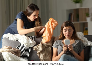 Angry Woman Scolding To Her Messy Roommate Sitting On A Couch In The Living Room At Home