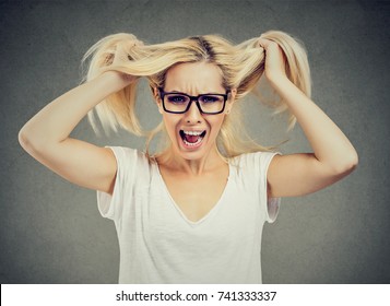 Angry woman screaming out loud and pulling her hair out isolated on gray background