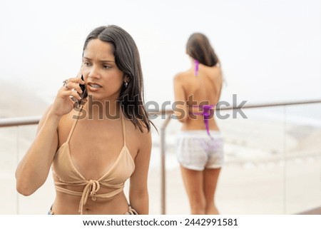 Angry woman talking to the mobile while a friends gazing sea views in a balcony