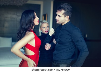 Angry Woman Threatens Disloyal Man Flirting And Looking Amazed To Another Seductive Girl In Red Dress