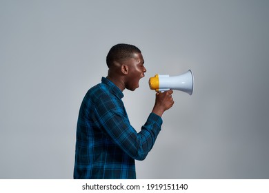 Angry young african american male protester, activist looking away, screaming using megaphone, posing isolated over gray background. Social issues, protest concept. Side view