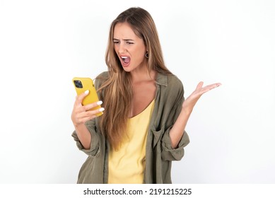 Angry Young Beautiful Woman Wearing Green Overshirt Over White Background Screaming On The Phone, Having An Argument With An Employee. Troubles At Work.