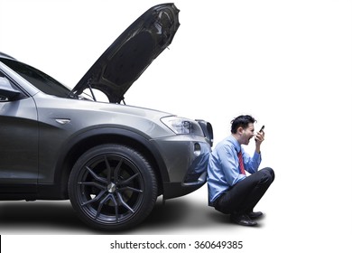 Angry young businessman using phone by broken down car, isolated on white background
