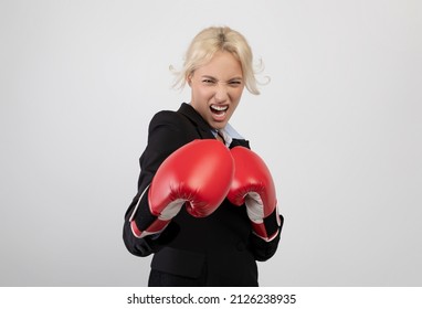 Angry young businesswoman in boxing gloves ready for fight over light grey studio background. Female office worker in formalwear preparing for combat, challenging competitors