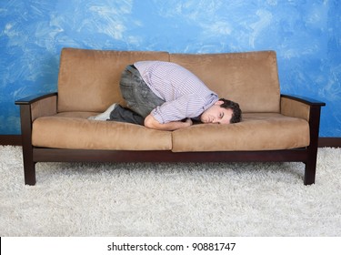 Angry Young Caucasian Man In Fetal Position On Sofa