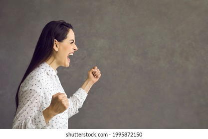 Angry young caucasian woman with clenched fist screaming showing furious face side view studio portrait. Irritated crying emotional female facial expression. Negative human emotions concept