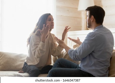 Angry young couple sit on couch in living room having family fight or quarrel suffer from misunderstanding, millennial husband and wife dispute involved in argument, relationships problems concept - Shutterstock ID 1646347387