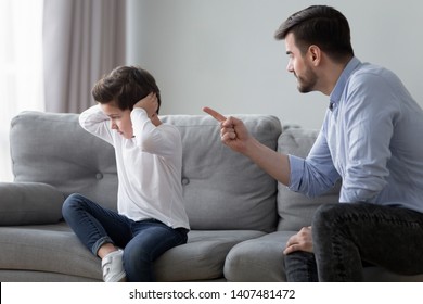 Angry Young Dad Sit On Couch Lecture Scold Preschooler Son Closing Ears With Hands, Offended Stubborn Boy Child Avoid Ignore Listening To Serious Mad Father Talking, Having Dispute Or Quarrel At Home