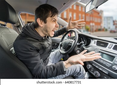 Angry young driver is driving a car and shouting.