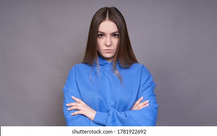 An Angry Young European Woman, Dressed In A Blue Sweatshirt, Holding Her Hands Folded, Looking At The Camera With A Strict And Skeptical Expression, Does Not Believe.