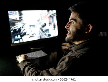 Angry Young Gamer Playing Videogame On Computer In Dark Room