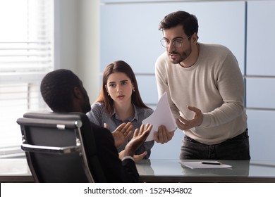 Angry young male customer dissatisfied with contract terms of conditions, shouting at african american lawyer bank worker or real estate agent. Millennial family couple disappointed with bad offer.
