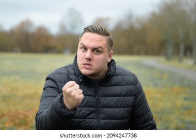 Angry young man menacing the camera with his fist as he scowls with a baleful glare outdoors in an autumn park - Shutterstock ID 2094247738