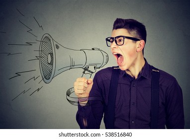 Angry young man screaming in megaphone isolated on gray background. Negative face expression emotion feeling. Propaganda, breaking news, power of social media concept