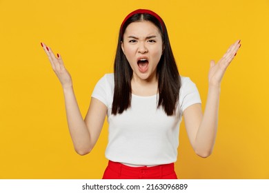 Angry Young Woman Of Asian Ethnicity She 20s Years Old Wears White T-shirt Looking Camera Scream Spreading Hands Isolated On Plain Yellow Background Studio Portrait. People Emotions Lifestyle Concept