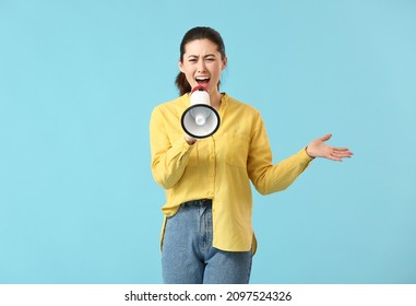 Angry young woman with megaphone on color background