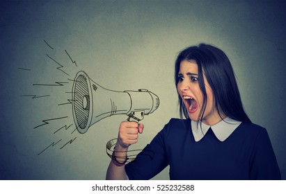 Angry young woman screaming in megaphone isolated on gray wall background. Negative face expression emotion feelings. Breaking news, power, social media communication concept