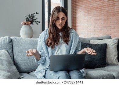 Angry young woman sit on sofa in living room frustrated having operational problems working on laptop, mad millennial girl feel stressed confused with slow internet connection or computer spam